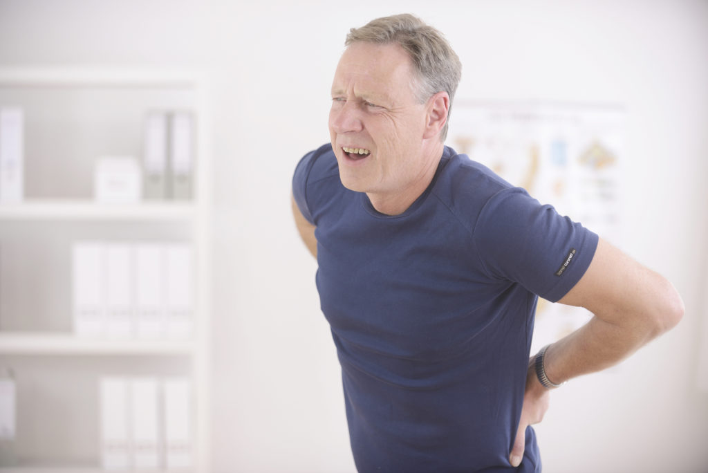 Etwas älterer Mann im blauen Hemd, der sich wegen Rückenschmerzen den Rücken hält
